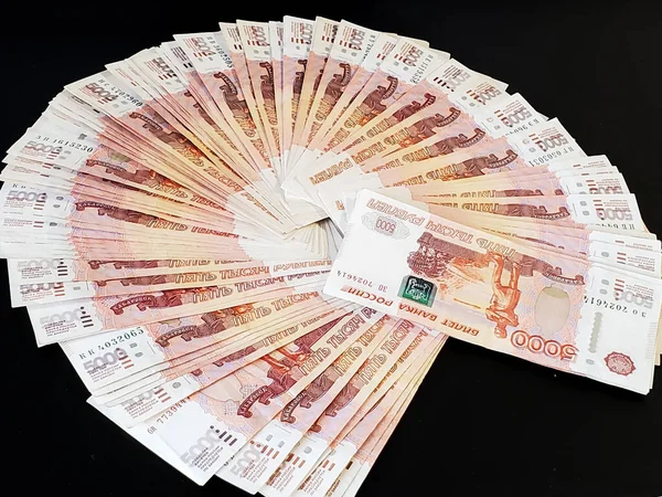 Russian money is fanned out on a black background. Russian banknotes