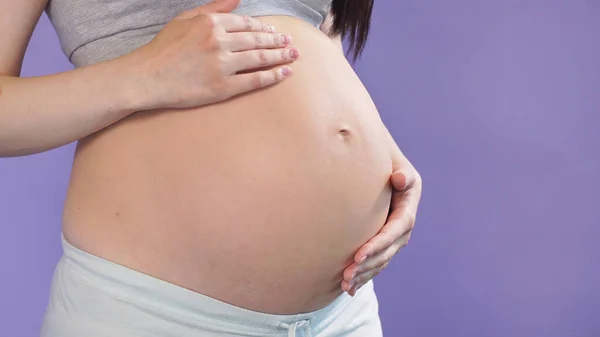 woman 9 months pregnant holds her tummy while posing in a Studio against an isolated background