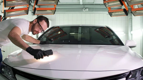 Man in gloves car polishing specialist checks the result of polishing with a flashlight