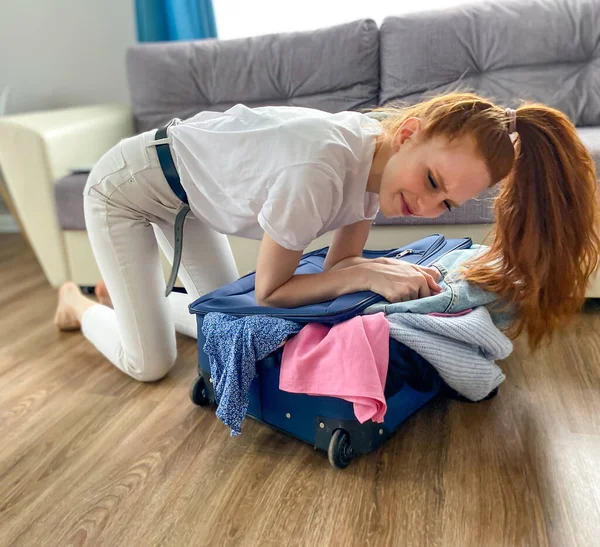 red-Haired girl wants to go on vacation, travel. A woman with a travel suitcase and a smartphone is going to go on vacation. The concept of vacation, travel