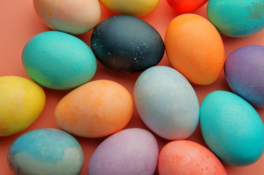 Renkli yumurtalar ve şekerler pembe arka planda yatar..