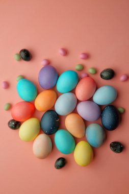 Renkli yumurtalar ve şekerler pembe arka planda yatar..