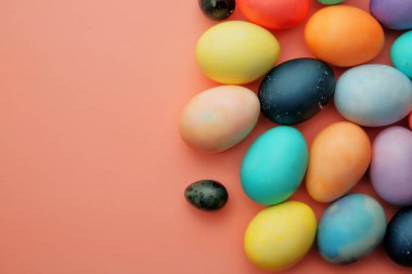 Renkli yumurtalar ve şekerler pembe arka planda yatar..