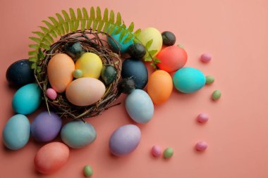 Paskalya 'da, eğreltiotu filizli pembe arka planda bir yuvada çok renkli yumurta ve lolipoplar..