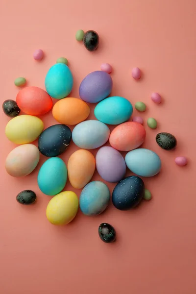 五彩斑斓的鸡蛋和糖果躺在粉色的背景上 — 图库照片