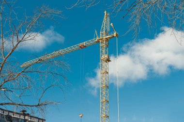 Mavi gökyüzü ve bulutlar arasında sarı kule vinci. Çok katlı binanın inşaatı.