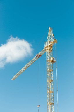 Mavi gökyüzü ve bulutlar arasında sarı kule vinci.