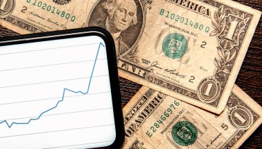 Masada dolar ve Amerikan para biriminin dinamiklerinin grafiği olan bir telefon var. Dolar büyümesi kavramı