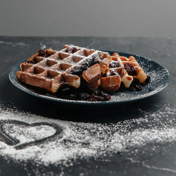 Vienna waffles sprinkled with sugar powder with a heart pattern, on a dark background, space for copying