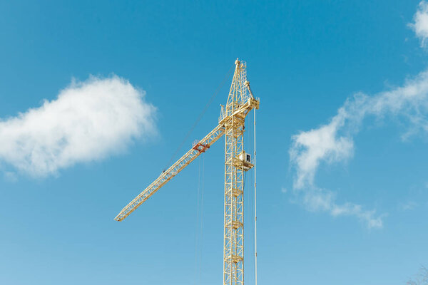 Yellow tower crane amid blue sky with clouds.