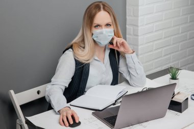 Maske takan ciddi bir kız kameraya bakar ve iş yerinin arkasında oturur.