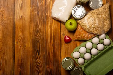 Coronavirus karantinası sırasında yiyecek teslimatı: konserve yiyecek, mısır gevreği. Uzun vadeli yiyecek depolama ve temel ihtiyaçlar ahşap arka planda yakın plan. Düz yatıyordu