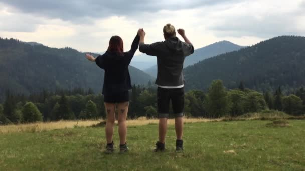 Young couple rase hands among the mountains — Stock Video