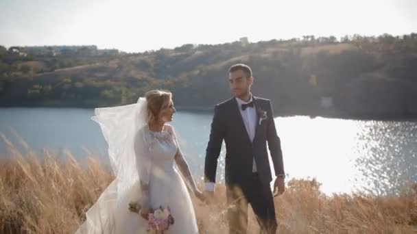 Невеста и жених прогуливаются вдоль реки — стоковое видео