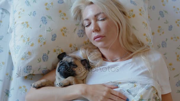 Mujer abrazando el cachorro pug tendido en la cama — Vídeos de Stock