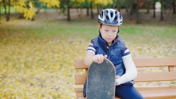 Blanke jongen met gebroken arm zit met skate — Stockvideo