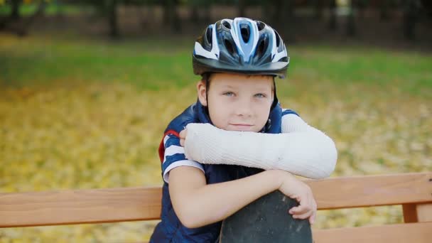 Biały chłopiec ze złamaną rękę siedzi z skate — Wideo stockowe