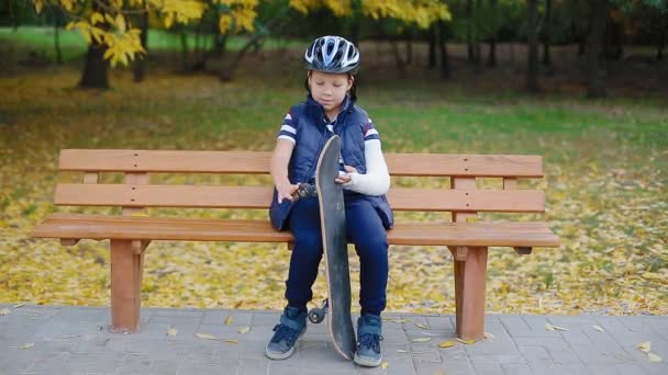 Vit pojke med bruten arm sitter med skate — Stockvideo