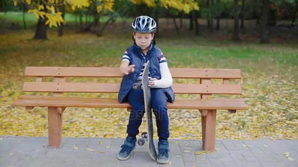 Biały chłopiec ze złamaną rękę siedzi z skate — Wideo stockowe