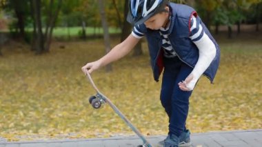 Kırık kol ile beyaz çocuk bir hüner üstünde paten yapmaya çalışın