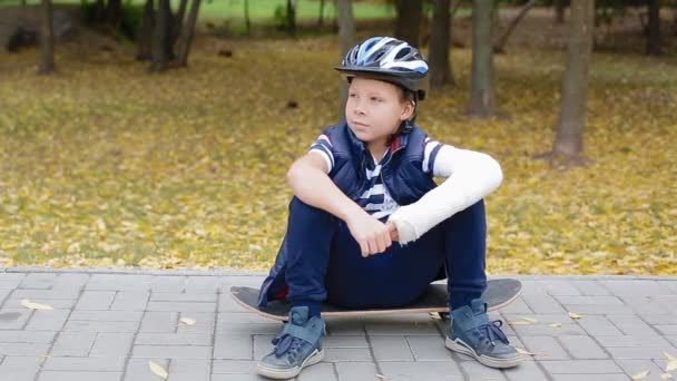 Niño blanco con el brazo roto sentado en su patín — Vídeo de stock