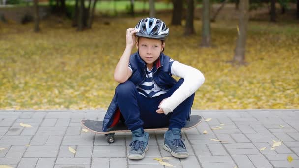 Niño blanco con el brazo roto puesto de su casco — Vídeo de stock