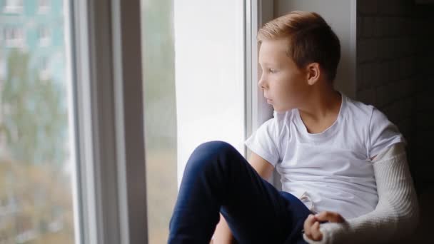 Szomorú fiú törött kézzel nézi az ablak — Stock videók