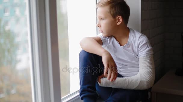 Sad boy with broken hand looking at the window — Stock Video