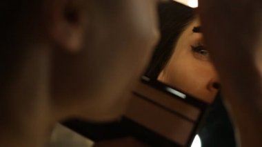 Kadın maskara uygulayarak ve aynaya bakıyor