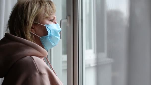 Женщина в медицинской маске на лице у окна — стоковое видео