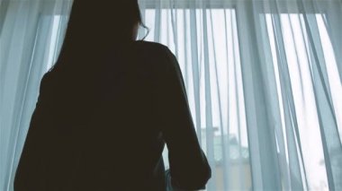 Genç kadın silueti mavi perdeleri açıyor.