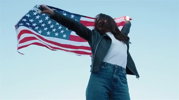 Ung kvinna viftar amerikansk flagga mot den blå himlen — Stockvideo
