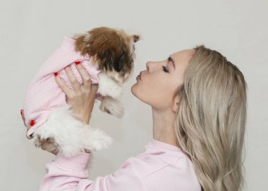 Güzel sarışın kız pembe elbiseli şirin bir shih tzu köpeğiyle açık arkaplanda