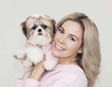 Güzel, şirin bir kız elinde pembe kazaklı Shih Tzu köpeği tutuyor.