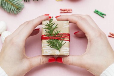 El yapımı, güzel kırmızı manikürlü kadın elleri pembe arka planda paketlenmiş bir hediyeyi gösteriyor.