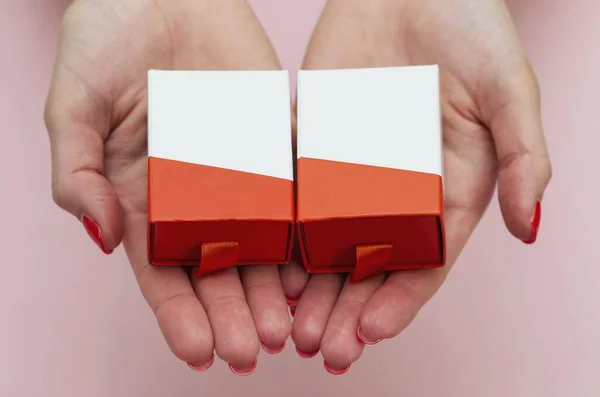 İki kadın avucunun içinde pembe arka planda birbirine benzeyen iki hediye kutusu var.