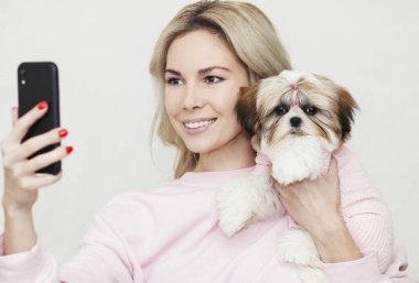 Kız, Shih Tzu köpeğiyle selfie çekiyor, telefonda poz veriyor, aynı şekilde giyinmiş.