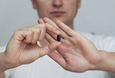 Adam elinde siyah bir hap tutuyor, eliyle ağzını kapatıyor, ilacı reddediyor, protesto ediyor.,