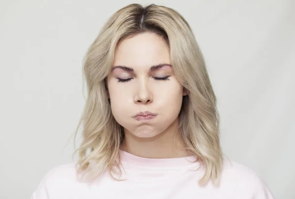 Komik, güzel, sarışın kız kameraya surat asıyor, şakacı davranışlar sergiliyor, pembe arka plan.