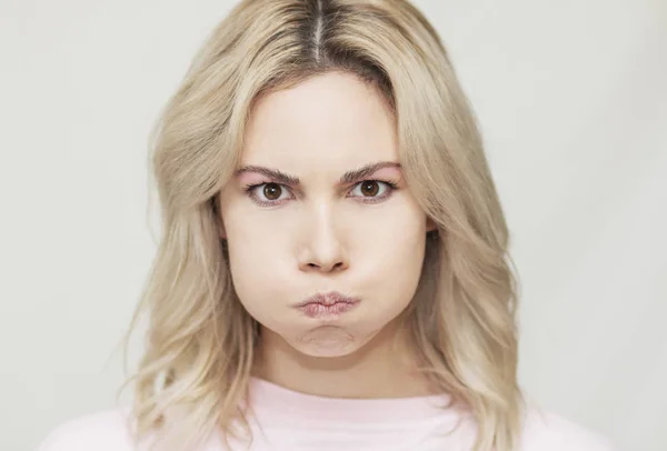 Komik, güzel, sarışın kız kameraya surat asıyor, şakacı davranışlar sergiliyor, pembe arka plan.