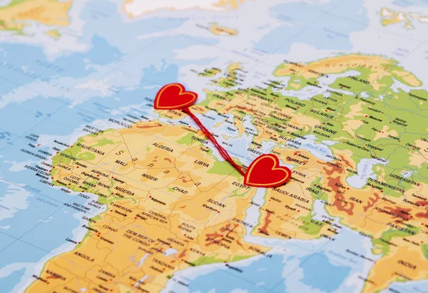 two red hearts on a world map connected by a red thread