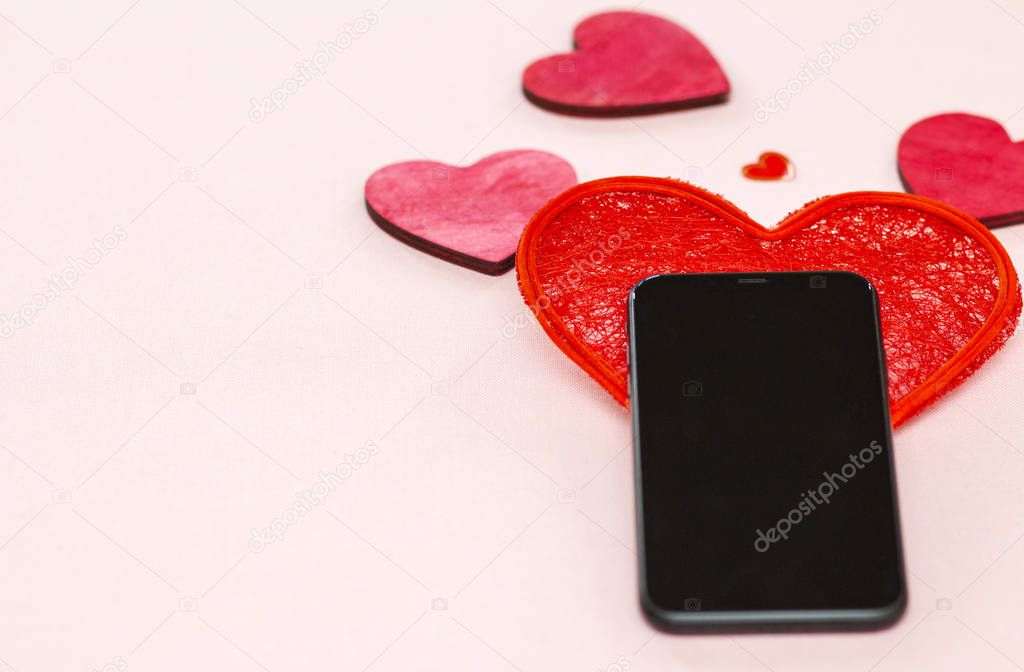 mobile phone lies on a red heart with a ribbon on a light background