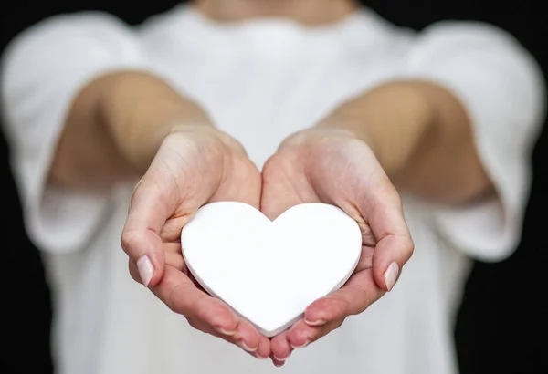 Adamın elinde beyaz bir kalp var, arka planda hafif giysiler var.