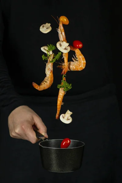 Taze iştah açıcı karides siyah bir arka planda siyah bir tavaya düşer.