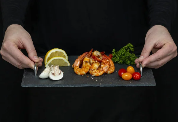 Erkekler taze, lezzetli karidesleri siyah tepside taşır.