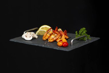 Siyah arka planda sebzeli lezzetli karidesli siyah tepsi.