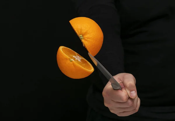 Adam siyah arka planda uçarken bir portakal kesiyor.