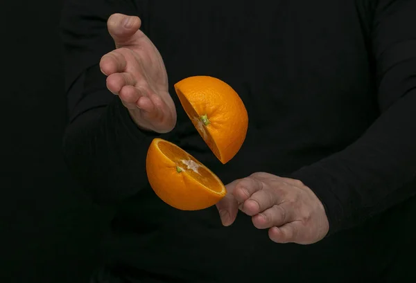 Bir adam elleriyle portakalı ikiye böler.
