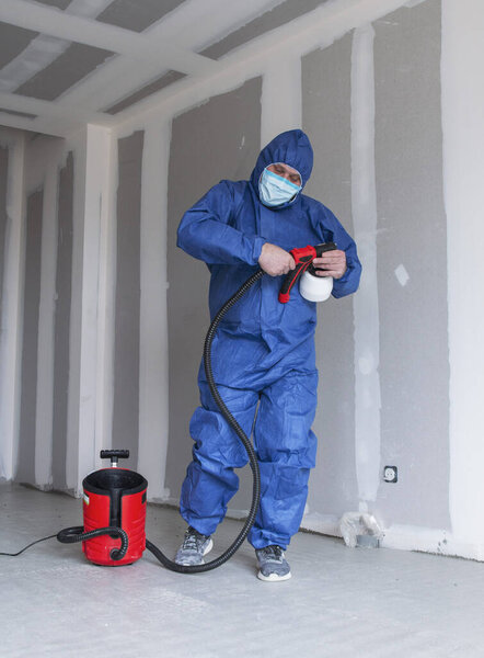 man in a special suit paints walls with a spray gun, painting walls and ceilings