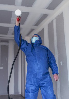 Özel takım elbiseli bir adam duvarları sprey silahla boyuyor, duvarları ve tavanları boyuyor.